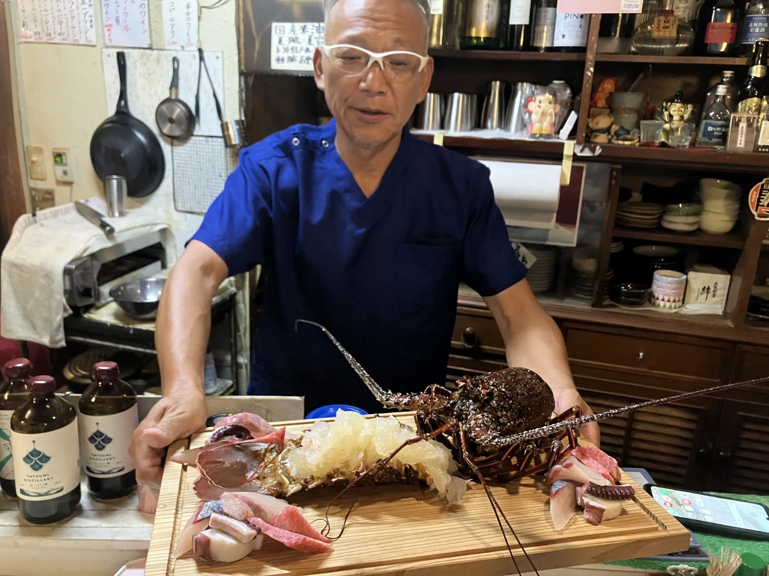 天花の店主が伊勢海老と刺身の盛り合わせをカウンターで紹介する様子